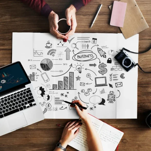 Content creators developing influencer education and training strategy using laptop, notes, and creative sketches on a desk.